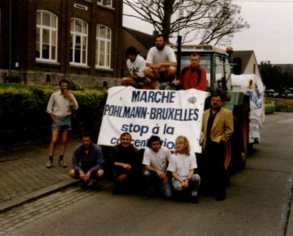 Des militants sont assis devant un tracteur qui arbore une banderole "marche Pohlmann-Bruxelle, stop à la concentration".