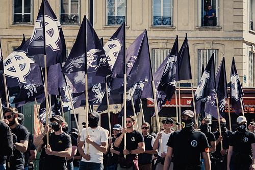Plusieurs rangées de militants d'extrême droite portant des drapeaux arborant une croix celtique blanche sur fond noir