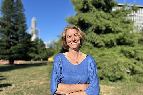 Une femme souriante croise les bras en regardant l'objectif dans un parc ensoleillé
