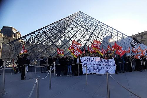 Des personnes portant des drapeaux CGT devant la Pyramide du Louvre. 