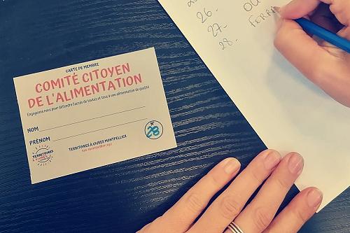 des mains écricent à côté d'une carte "comité citoyen de l'alimentation" posées sur une nappe bleue