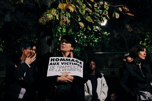 Une manifestante tient une banderole sur laquelle il est écrit « hommage aux victimes de Trappes et la Verrière »