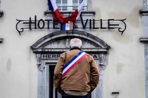Un maire, de dos devant son hôtel de ville, avec son écharpe tricolore