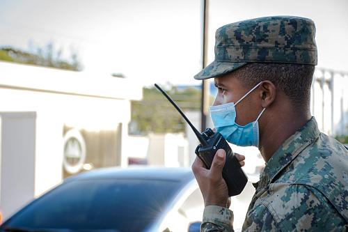Un homme en tenue militaire de profil tient un talkie-walkie.