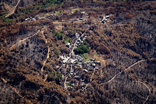 Une photo aérienne de deux hameaux de maisons en partie calcinées au milieu d'un paysage d'arbres eux aussi brûlés.