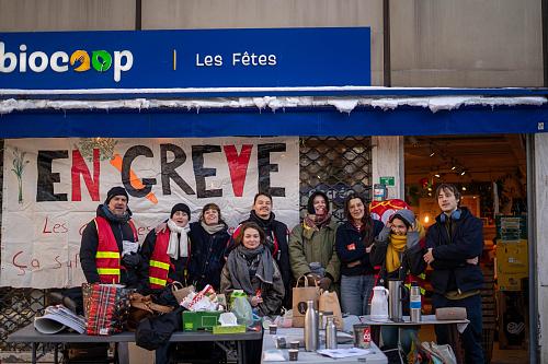 Photo de groupe des grévistes devant l'enseigne Biocoop "Les Fêtes". Ils sont neufs. Derrière eux on aperçoit une banderole "en grève". 