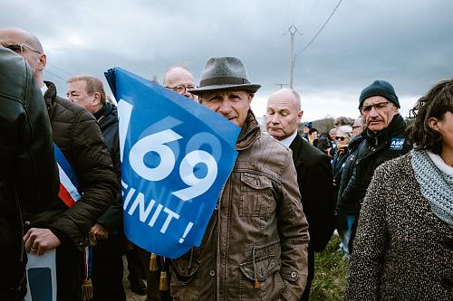 Un homme avec un drapeau "A69 on finit" sur fond bleu