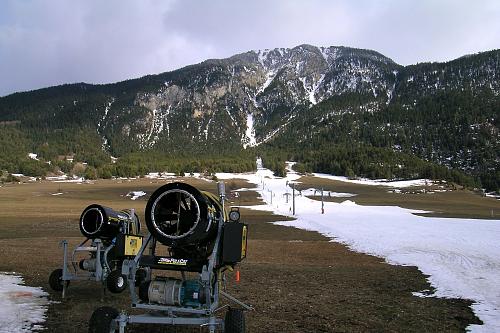 Canons à neige sur fond de paysage montagnard en manque de couverture neigeuse.