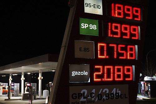 Une station essence de nuit en arrière plan, les prix affichés au premier plan. 