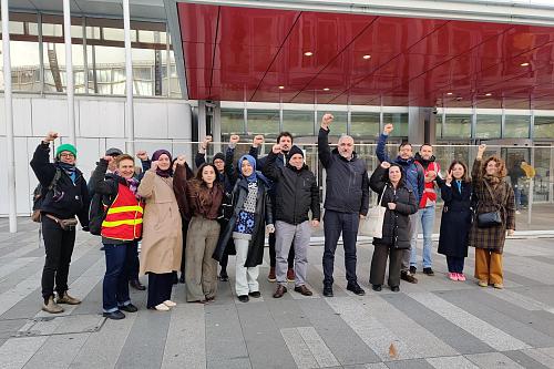 Une douzaine de personnes debout devant le bâtiment du tribunal judiciaire de Paris levant le poing. 