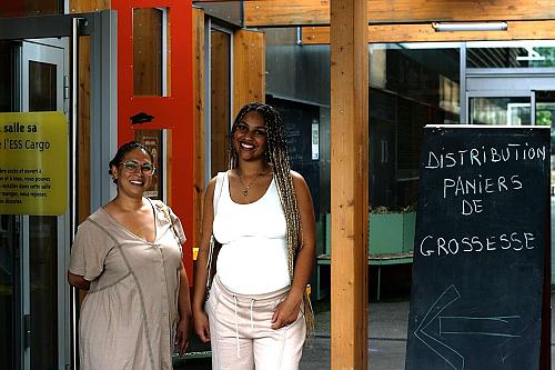 Deux femmes enceintes sourient, à côté d'un tableau affichant "distribution paniers de grossesse"