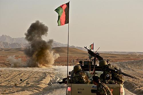 Une voiture militaire sur une route, avec un drapeau de l'Afghanistan qui flotte au-dessus et une explosion à quelques mètres.
