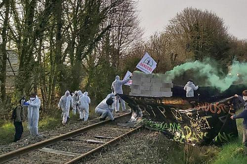 des militants vêtus de combinaisons blanches érigent un mur de parpaings sur des voies ferrées