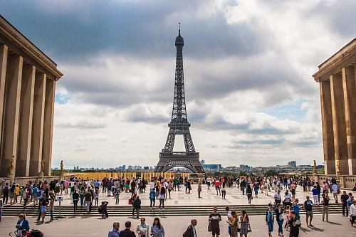 Vue du parvis devant la tour Eiifel, plein de monde qui déambule. 