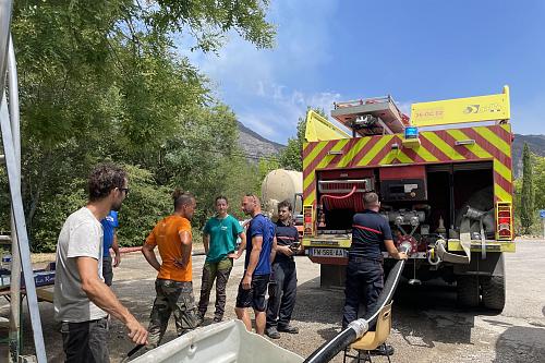 Un camion de pompier tire de l'eau d'une cuve, au milieu d'habitants et de quelques pompiers. 