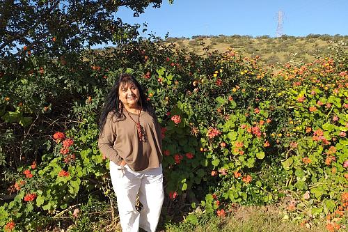 Une femme souriante devant une haie fleurie. 