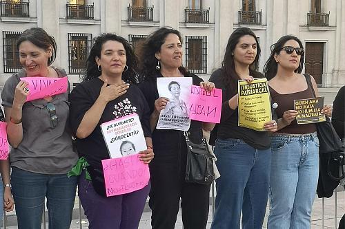 Des femmes debout dehors tiennent des feuilles sur laquelle on voit l'image d'une femme et des slogans. 