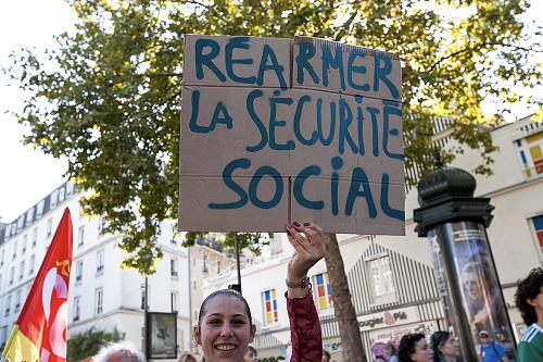 Une jeune femme tient une pancarte sur laquelle il est écrit "Réarmer la Sécurité sociale"