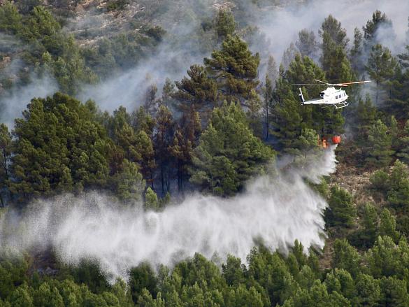 Un hélicoptère survole une forêt en flammes. 