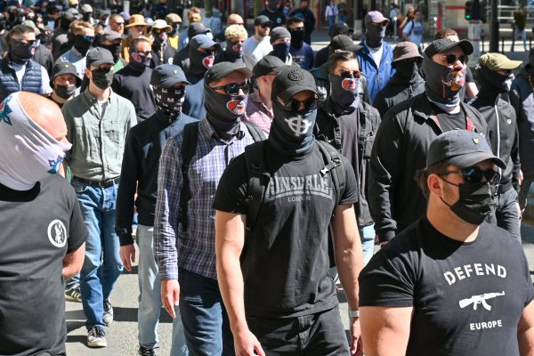 Militants d'extrême droite défilant en rang, masqués, arborant des croix celtiques ou des tee-shirts "Defend Europe" avec un fusil d'assaut.