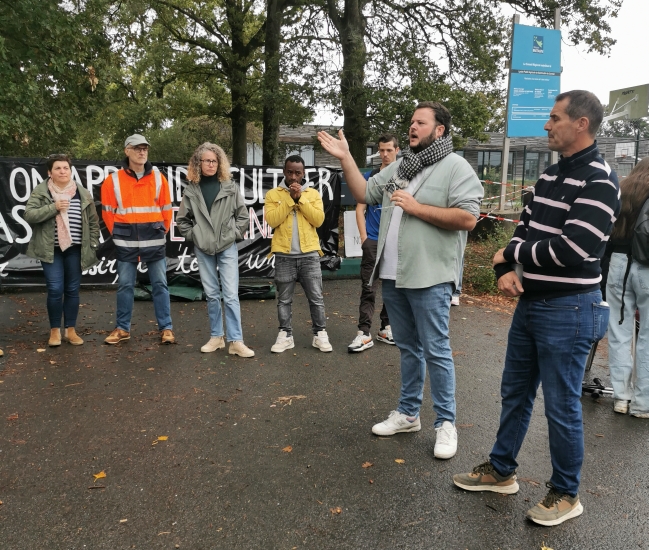 un homme parle dans un micro devant cinq personnes debout.