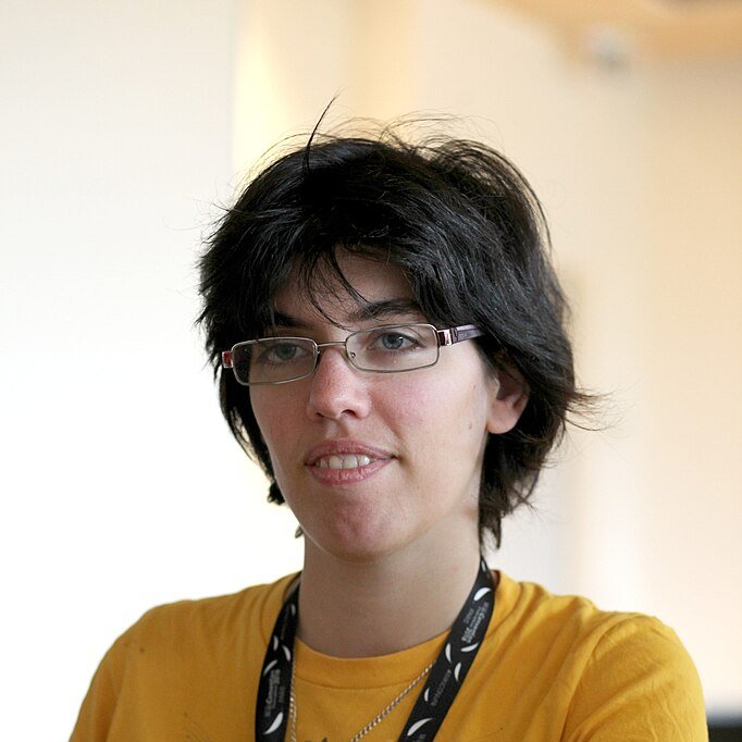 Photo portait d'une personne aux cheveux bruns, lunettes et t-shirt jaune