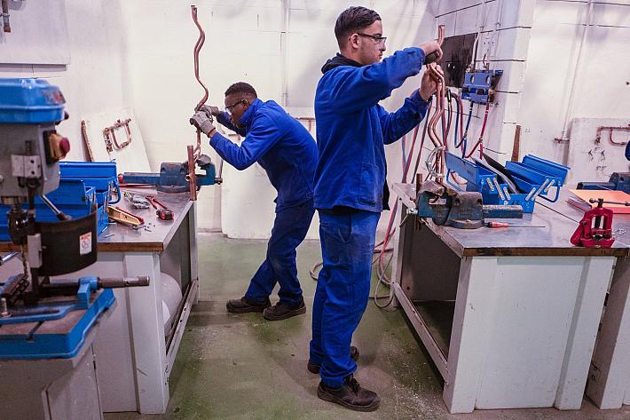 Deux jeunes garçons en bleu de travail examine des tubes de cuivre.