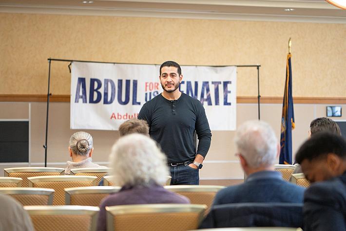 Abdul El-Sayed en jean et tshirt dans une salle, debout face à des peronnes assises, vues de dos.
