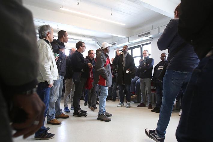 Des hommes debout dans une salle, l'un d'entre eux parle.