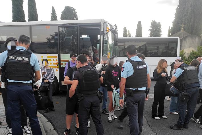 En rang, des gendarmes fouillent des lycéens, en arrière plan on aperçoit des bus.