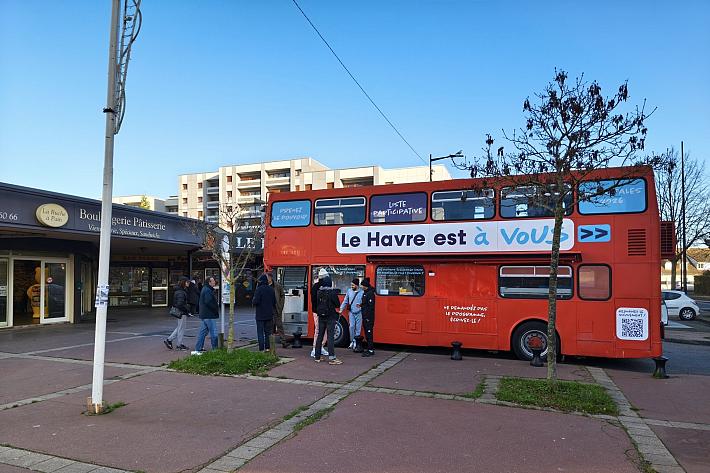 Un bus rouge à deux étages sur un parking, des personnes entrent dans le bus. 