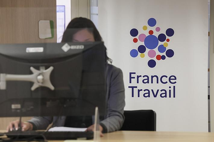 Une femme est assise derrière un écran, devant le logo de France Travail.