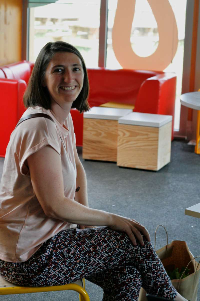 Une femme souriante, assise, regarde l'objectif.