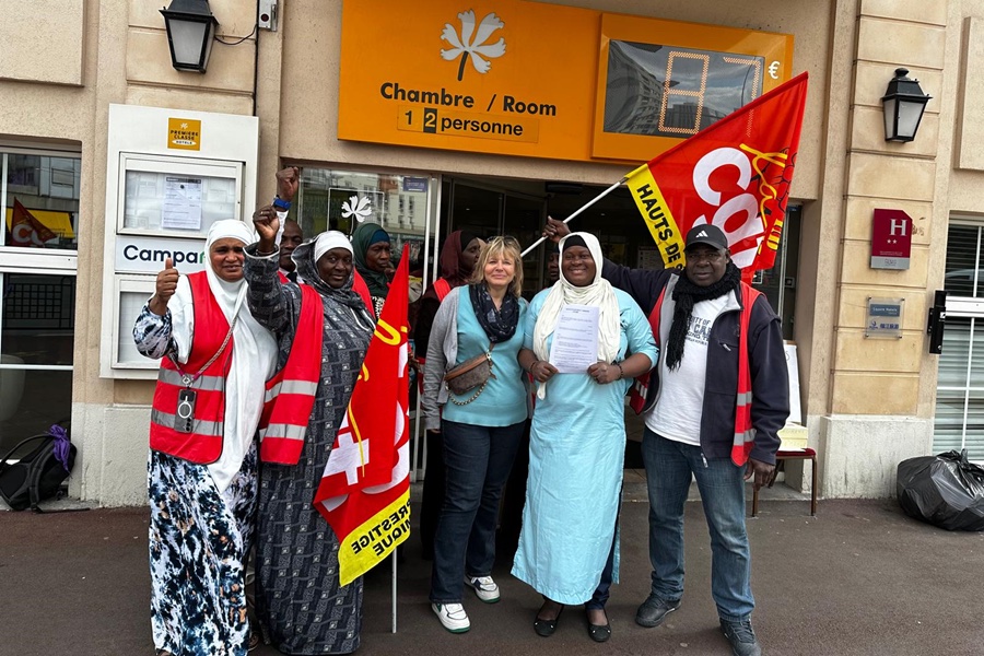 Six femmes et deux hommes devant la devanture d'un hôtel, L'une tient un drapeau CGT. 