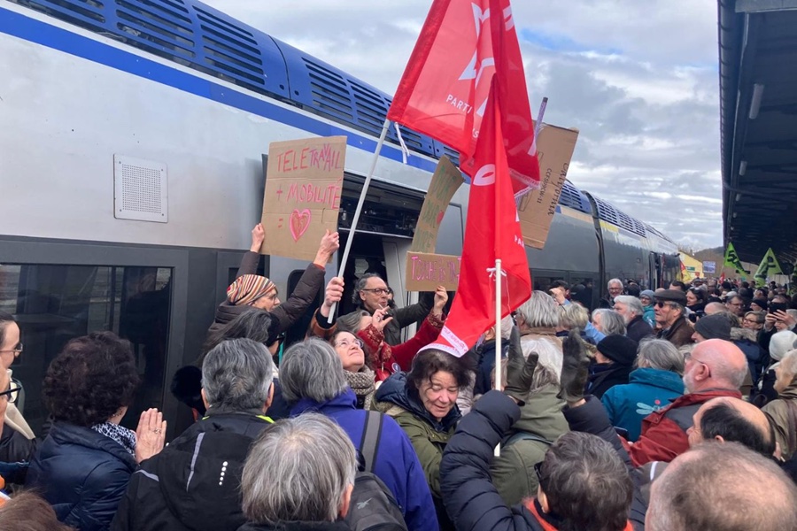 Des dizaines de personnes amassées sur un quai de gare à la sortie d'un train, certaines tiennent des pancartes et d'autres des drapeaux rouges.