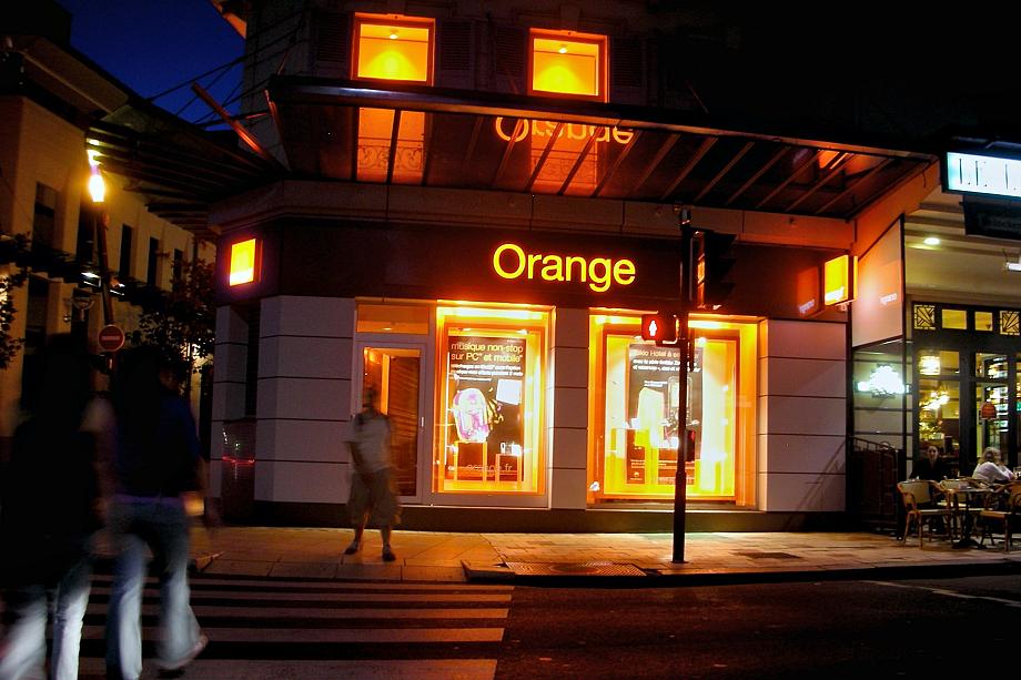Une boutique Orange dans une ville la nuit, le nom “Orange” est illuminé en orange.
