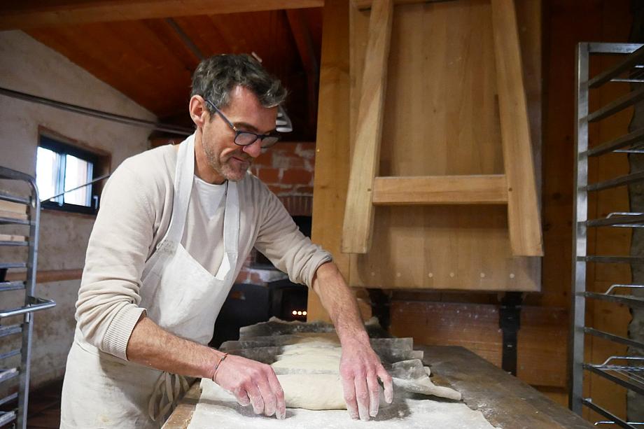 Un homme avec un tablier blanc façonne des pains au levain dans son fournil