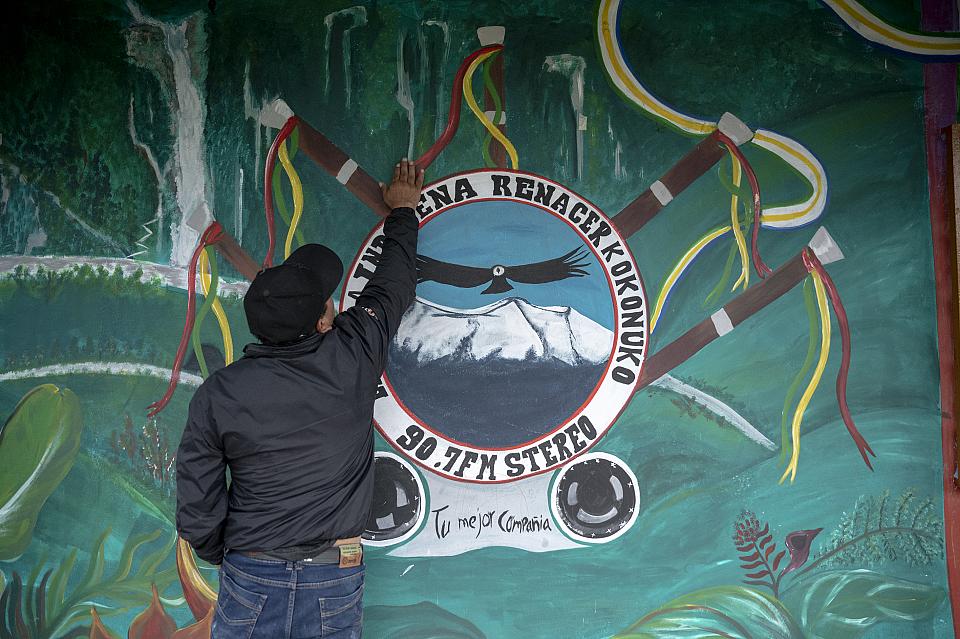 Un homme de dos montre un logo peint sur une façade.