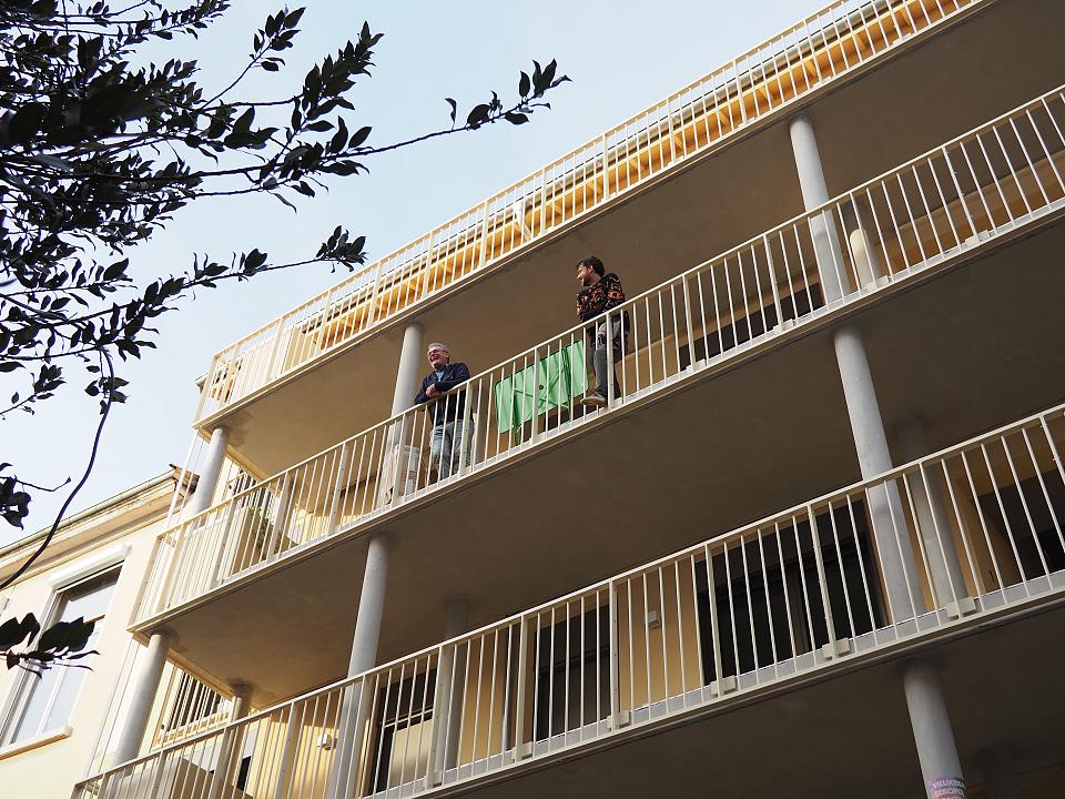 Vue du bâtiment en contreplongée. Deux personnes se trouvent à un balcon. 