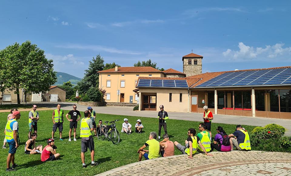 Des personnes en gilo fluorescents avec des vélos devant des bâtiments dont les toitures sont équipées de panneaux photovoltaïques.