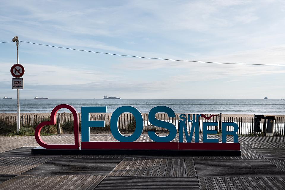 Le logo géant de la ville, sur le port de Fos-sur-Mer. En arrière plan, la mer, avec un défilé d'énormes navires de commerce. 