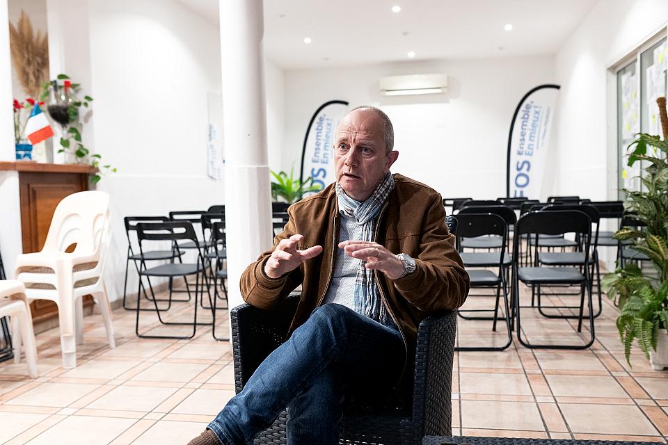 Le candidat de droite Phillipe Maurizot dans son local de campagne. Il porte un jean et une veste marron. Sur la gauche figure un petit drapeau bleu-blanc-rouge.