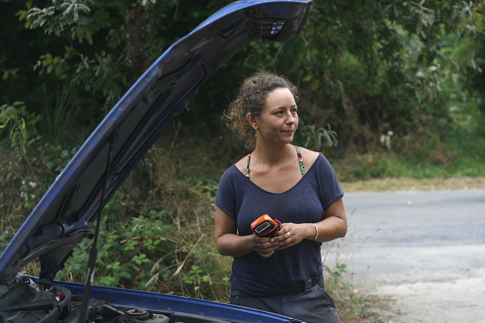 Une femme devant un capot de voiture ouvert 