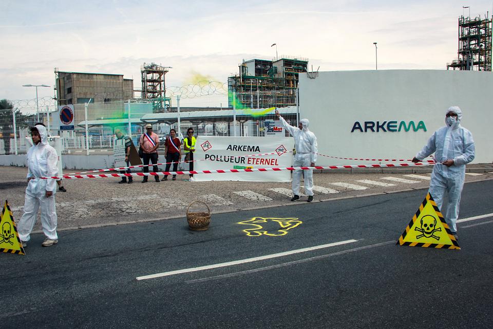 Trois personnes en combinaison blanche devant l'entrée d'une usine Arkema. 