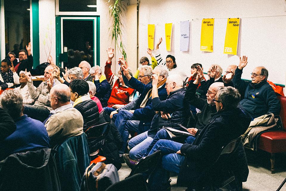 Une assemblée d'une trentaine de personnes, des gens lèvent la main. 