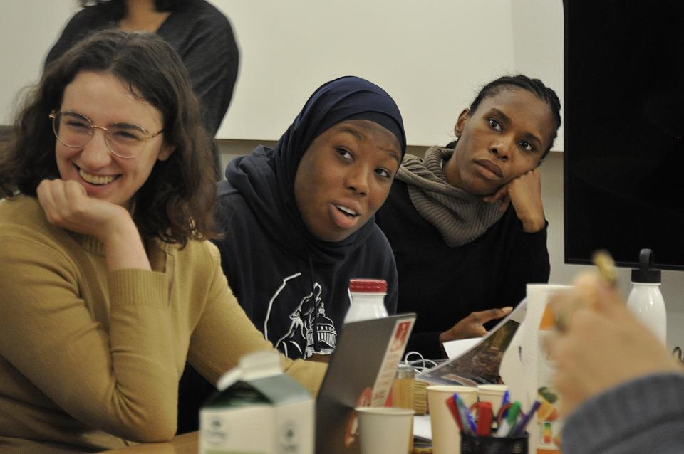 Trois femmes à une table, l'une sourit, un autre parle, une troisième écoute.