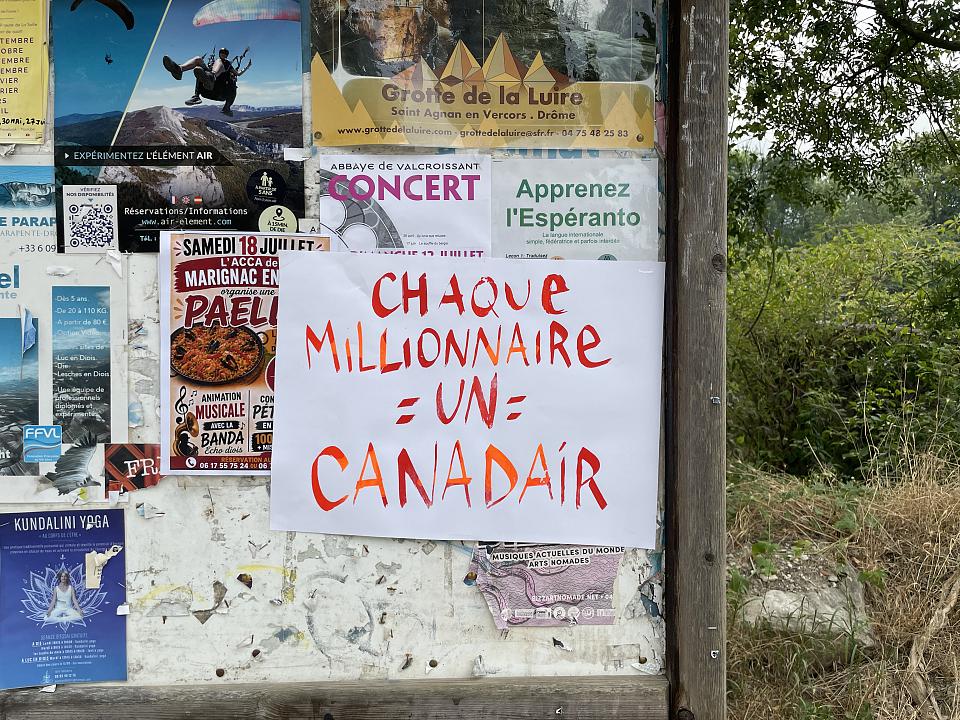 Une affichette sur laquelle il est écrit "Chaque millionnaire = un canadair" collée sur un panneau d'affichage municipal. 