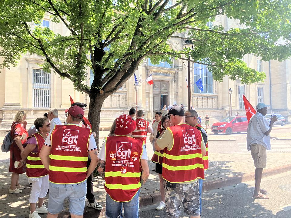 Des personnes avec des chasubles rouge CGT rassemblées devant le tribunal. 