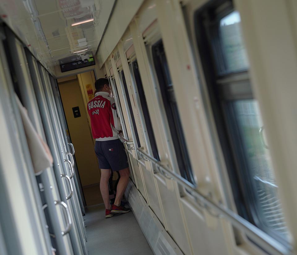 Dans le couloir d'un train, un homme porte une veste floquée « Russie ».