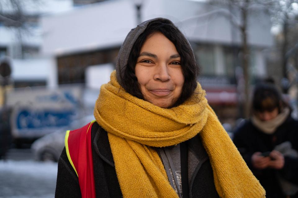 Femme capuchée vêtue d'une écharpe jaune et d'un gilet CGT. Elle sourit.